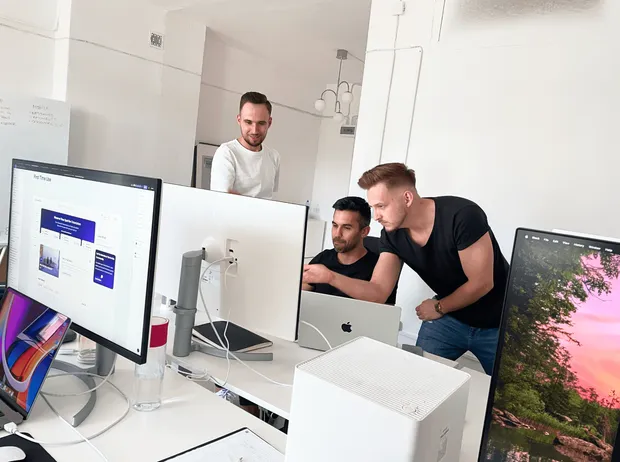 Three team members looking at designs on a monitor